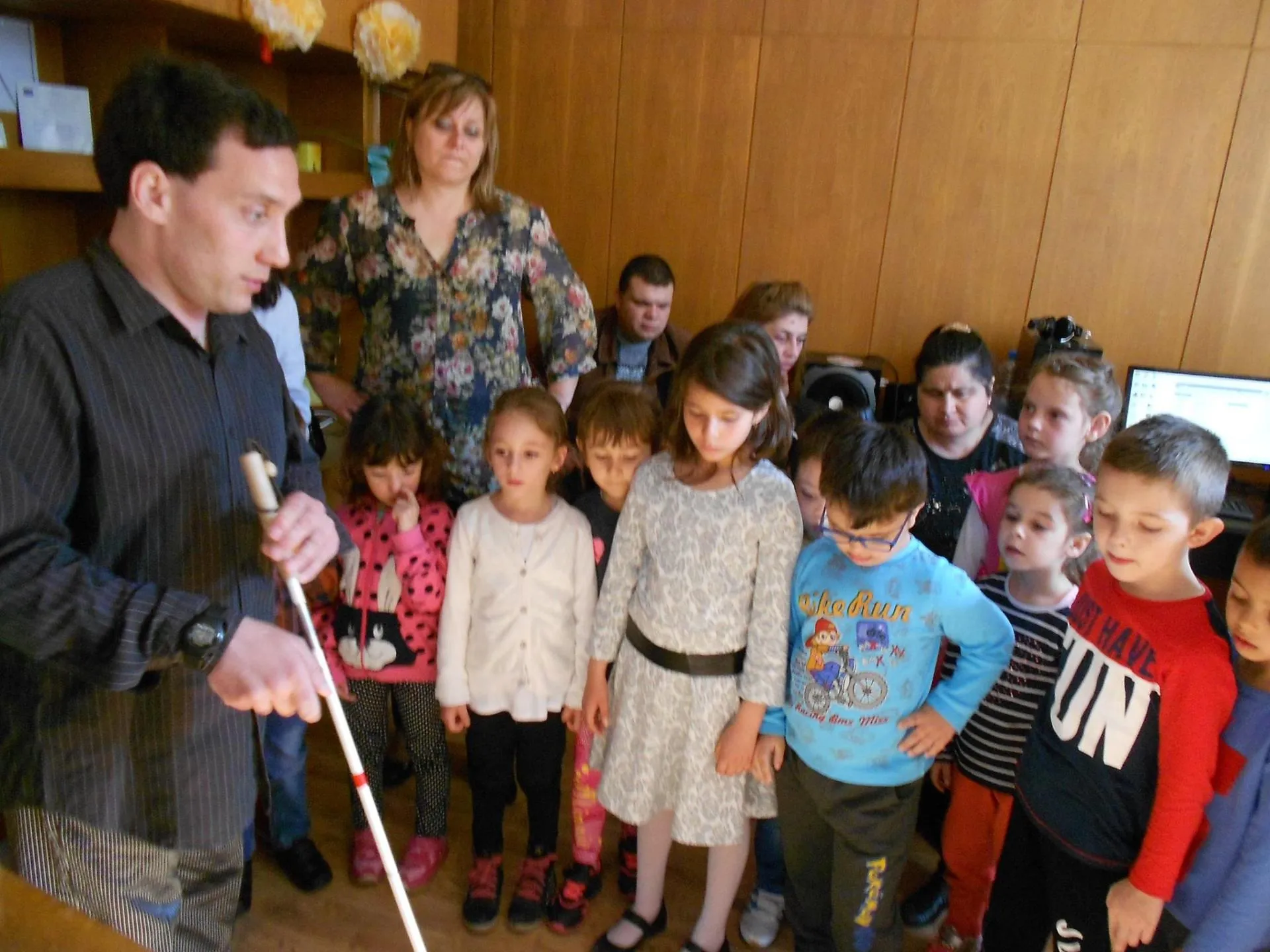 A man with a white cane demonstrates mobility techniques to a group of children at the Centre